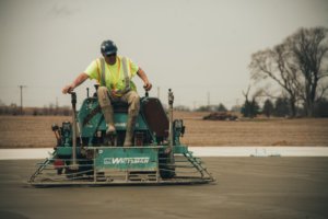 employee on a ride-on concrete trowel machine finishing a parking lot
